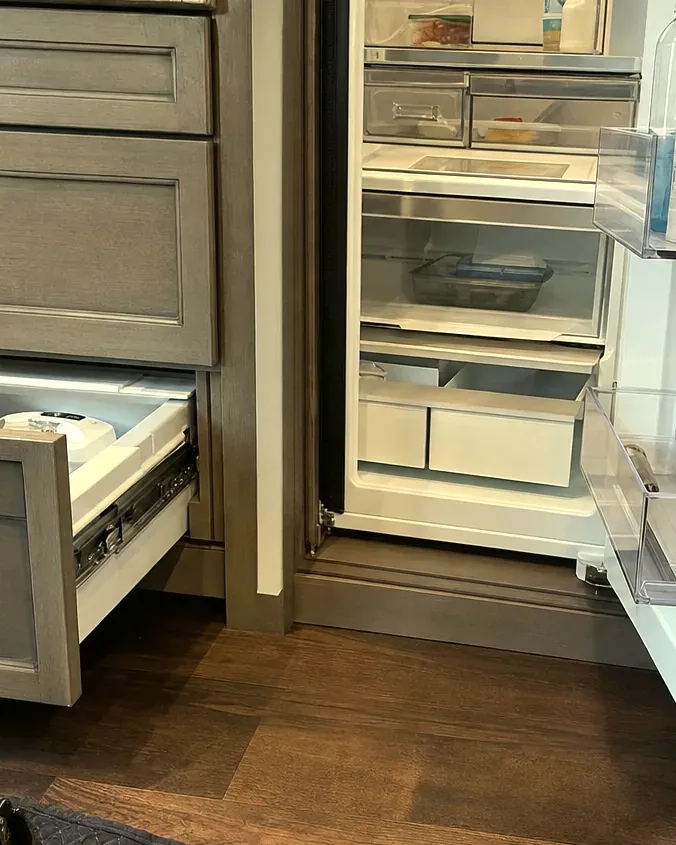 Built-in refrigerator standing open in grey kitchen cabinetry, its shelves and crisper drawers in view.