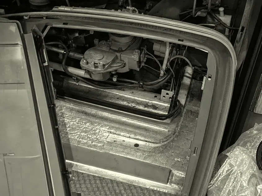 Monochrome view through an appliance's gasketed door opening into a stripped compartment, a motor assembly and wiring exposed inside.