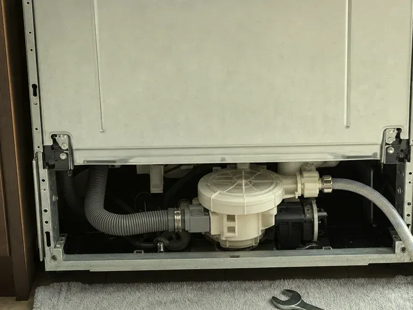 Dishwasher sump and drain hose under the tub, a wrench on the towel below.